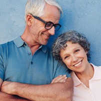 Fit and vibrant senior couple, arms linked, cheerfully posing for a photo in front of a textured blue wall.