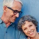 Fit and vibrant senior couple, arms linked, cheerfully posing for a photo in front of a textured blue wall.